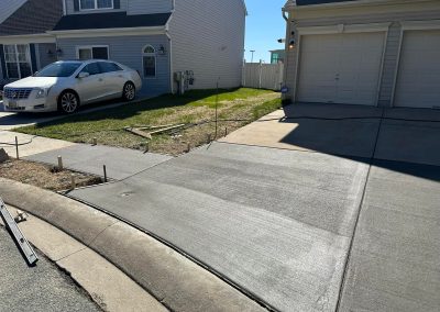 Freshly poured concrete driveway and sidewalk in front of a house, with a white car parked nearby.