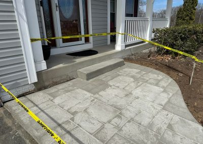 Freshly poured concrete patio cordoned off with yellow caution tape in front of a house entrance.