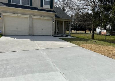 A house with a double garage, concrete driveway, and a grassy yard with some trees.