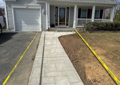A freshly paved walkway to a house, bordered by caution tape on both sides.