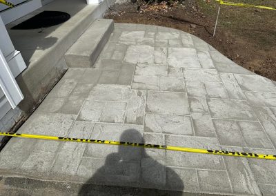 Freshly poured concrete patio with caution tape around it, in front of a house entrance.