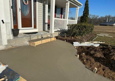 Fresh concrete has been poured to form a new walkway leading to the front porch of a house.
