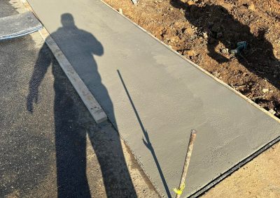 Freshly poured concrete sidewalk bordered by dirt, with a shadow of a person and a tool on the surface.