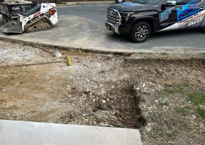 A construction site with dug-up ground, a sledgehammer, skid steer, and two parked vehicles nearby.