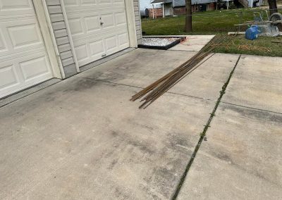 Several long metal rods are stacked on a driveway next to a closed double garage door.