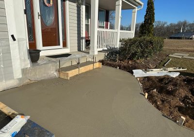 Fresh concrete is poured for a curved walkway leading to a house entrance with a porch.