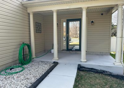 A house front porch with columns, a green hose, and a glass door, leading to a concrete walkway.