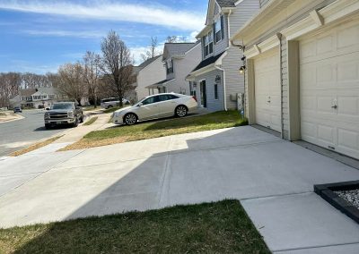 A white car is parked on a sloped lawn beside a suburban house on a sunny day.
