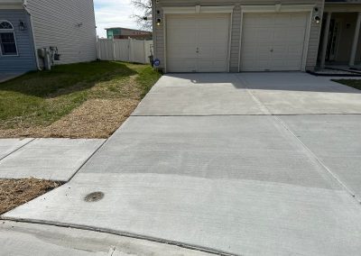 A concrete driveway leads to a two-car garage beside a patch of grass and a sidewalk.