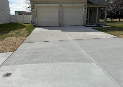 A clean, wide concrete driveway leads to a two-car garage attached to a beige house.