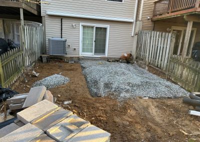 Backyard with gravel spread on the ground, pavers stacked, and construction materials next to a townhouse patio.