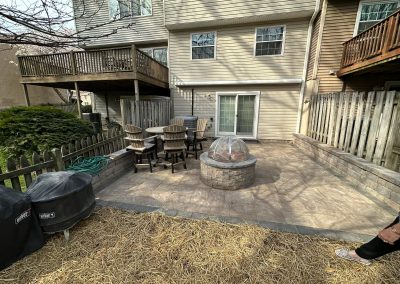 A backyard patio with a fire pit, chairs, grills, and a sliding glass door leading to the house.