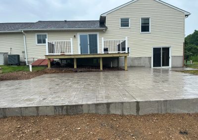 Wet concrete patio and raised deck behind a beige house with white trim on a cloudy day.