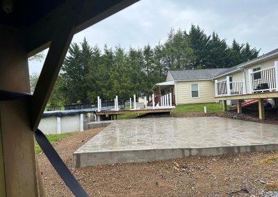 Freshly poured concrete slab in front of a house with trees and another building in the background.