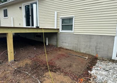 A backyard patio area under construction beside a deck and house with tools and building materials visible.
