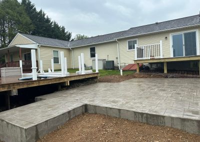 A backyard patio under construction with stamped concrete and unfinished decking near a light yellow house.