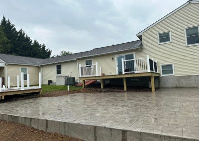 Backyard with a stamped concrete patio, two raised decks with railings, and a beige house in the background.