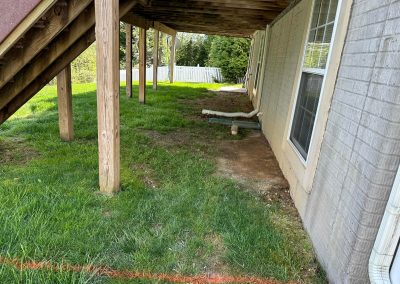 View under a wooden deck beside a house, with green grass and an orange line marking the ground.