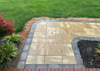 Wet stone patio with a dark border, surrounded by grass, mulch, and green plants.