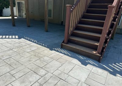 Concrete patio with a brown wooden staircase and shadows from the railing cast on the ground.