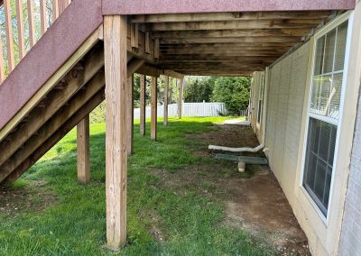Wooden deck stairs above a grassy yard next to a white brick house with a drainage pipe by the wall.