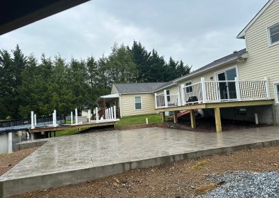 A house with a raised deck and a newly poured concrete patio under a cloudy sky.