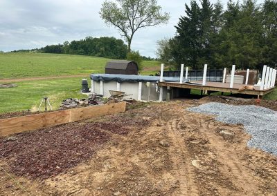 Dirt and gravel yard with construction materials beside an above-ground pool and trees in the background.