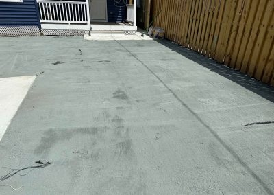 A freshly resurfaced concrete area beside a wooden fence, near a blue house with a white porch.
