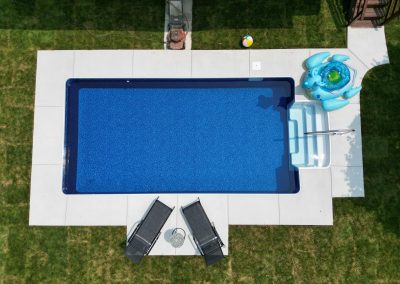 Aerial view of a backyard pool with pool chairs, a drink table, a float, and a beach ball on the grass.