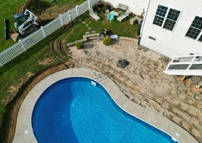 Aerial view of a backyard with a pool, patio furniture, and ongoing landscaping work near a white house.