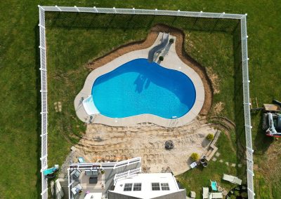 A fenced backyard with an irregular-shaped pool, patio, and yard under renovation, viewed from above.