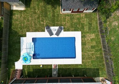 A backyard pool with two lounge chairs, pool floats, and green grass, viewed from above.