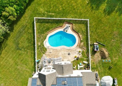 Aerial view of a backyard with a swimming pool, patio area, and solar panels on the house roof.