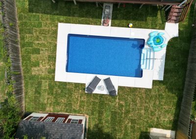 Aerial view of a backyard pool with lounge chairs, a float, and patchy green grass surrounding it.