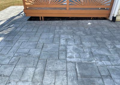 Stamped gray concrete patio with a decorative wooden railing in the background.