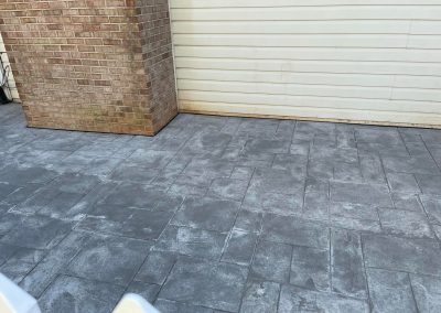 Gray stamped concrete patio near a brick wall and white garage door.