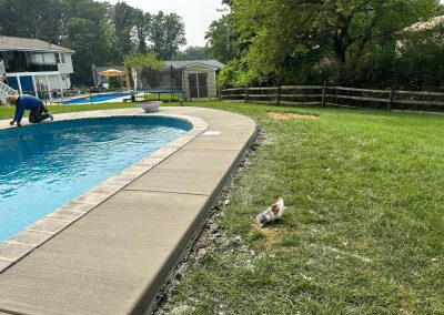 A person works near a backyard pool, with a plastic bottle discarded on the grass nearby.
