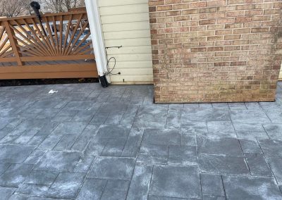 Gray stone patio with a brick wall, tan siding, and a brown wooden fence with sunburst pattern.