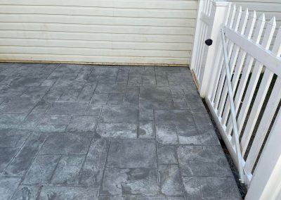 Gray stamped concrete patio beside a white fence and a cream-colored siding wall.