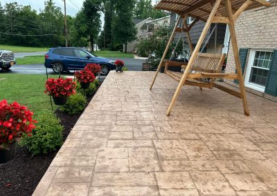 A patio with a wooden swing, potted red flowers, and a blue SUV parked in the driveway.