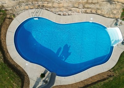 Aerial view of a kidney-shaped swimming pool with clear blue water and a concrete deck.