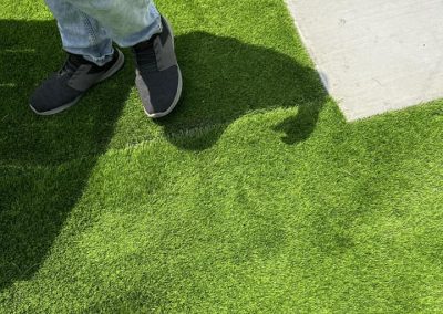 Person in jeans and sneakers standing on bright green grass, with distinct shadows visible on the ground.