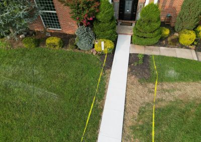 A concrete walkway leads to a brick house entrance, bordered by yellow caution tape and trimmed bushes.