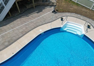 A clear blue swimming pool with white steps, surrounded by concrete and paver patio near a staircase.
