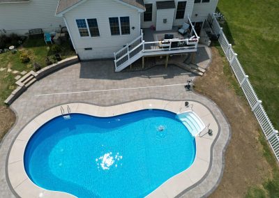 Aerial view of a backyard with an in-ground pool, patio, deck, and fenced grassy area.
