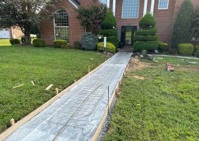A walkway covered in plastic and rebar is being prepared for concrete in front of a brick house.