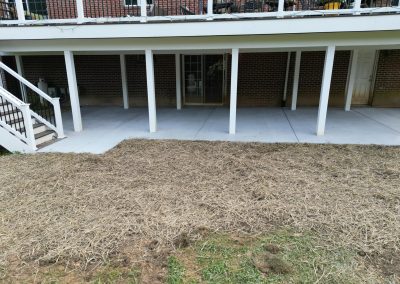 A covered patio with white columns and straw-covered ground leading up to a grassy area.