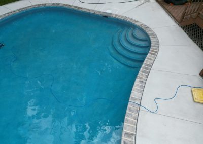 A swimming pool with curved steps, surrounded by concrete, and a blue cord lying on the ground.