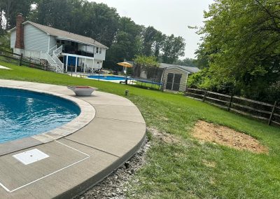 A backyard with a pool, grassy lawn, fenced yard, and a house with a deck in the background.
