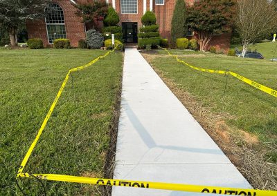 Freshly paved sidewalk leading to a brick building, bordered by yellow caution tape on both sides.